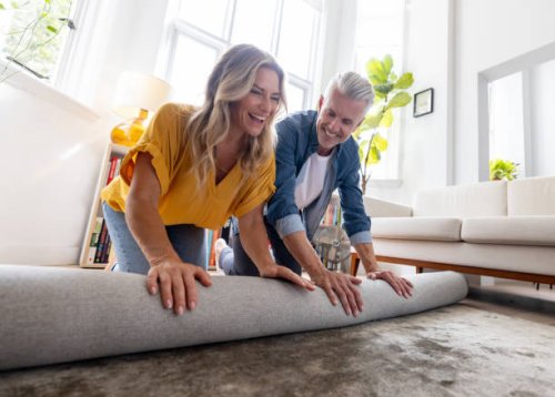 happy couple moving house and unrolling a carpet while unpacking - home decoration stock pictures, royalty-free photos & images