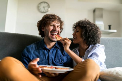 happy couple sitting on couch eating pizza - junk food stock pictures, royalty-free photos & images
