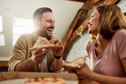 happy couple talking while eating pizza for lunch at home. - junk food stock pictures, royalty-free photos & images