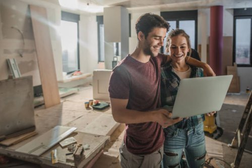 happy embraced couple using laptop while being on construction site in their apartment. - home decoration stock pictures, royalty-free photos & images