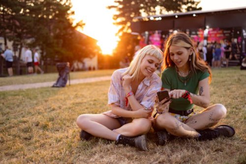 happy female festival goers using mobile phone at sunset. - concert stock pictures, royalty-free photos & images