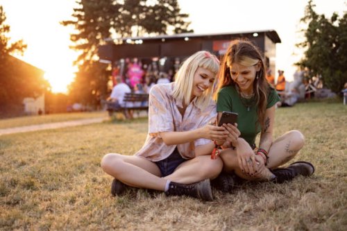 happy female festival goers using smart phone at sunset. - concert stock pictures, royalty-free photos & images