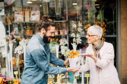 happy florist giving a flower bouquet to a smiling young man - garden decoration stock pictures, royalty-free photos & images