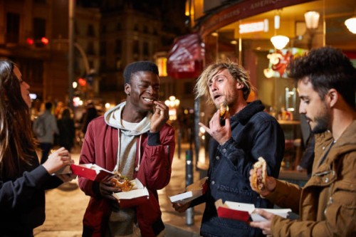 happy friends enjoying burger on street at night - junk food stock pictures, royalty-free photos & images