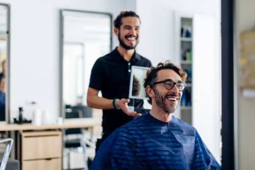 happy hairdresser showing haircut to client in mirror at salon - hairstyle photos et images de collection