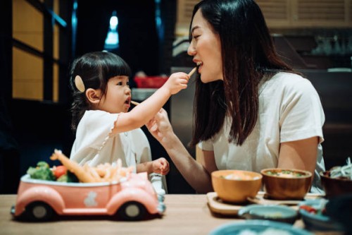 happy little asian girl enjoying her kids meal set with her mother in a restaurant. they are feeding each other with french fries and having a enjoyable time together - junk food stock pictures, royalty-free photos & images