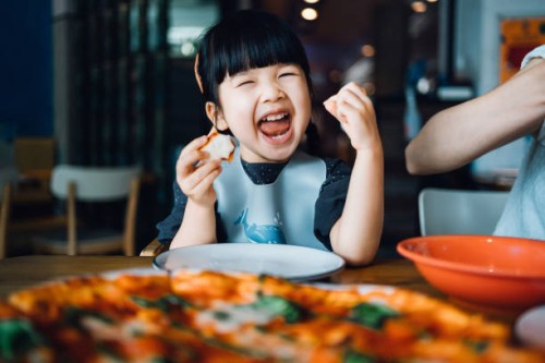 happy little asian girl enjoying pizza lunch in an outdoor restaurant, with a giant pizza in front of her on the dining table. looking at camera and smiling joyfully. eating out lifestyle - food stock pictures, royalty-free p