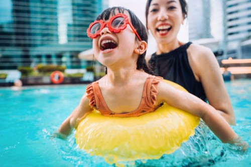 happy little asian girl with sunglasses smiling joyfully and enjoying family bonding time with mother, having fun in the swimming pool on summer vacations - travel stock pictures, royalty-free photos & images
