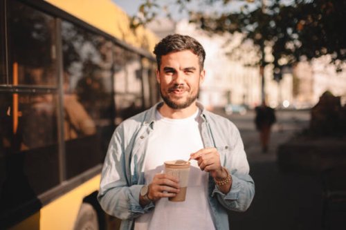 happy man holding cup of coffee while standing on street during summer - junk food stock pictures, royalty-free photos & images