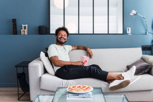 happy man spending leisure time sitting on sofa at home - junk food stock pictures, royalty-free photos & images
