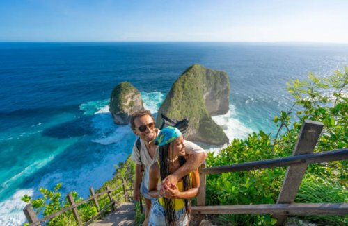 happy multiracial couple standing above kelingking beach, enjoying the view and taking selfies - travel stockfoto's en -beelden