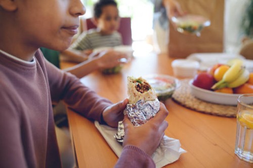 happy multiracial family sitting at dining table and having lunch at home. - junk food stock pictures, royalty-free photos & images