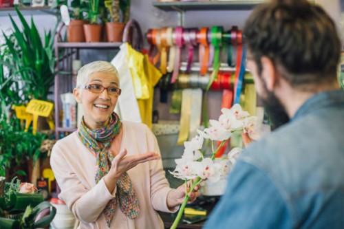 happy senior florist showing a flower to a customer - garden decoration stock pictures, royalty-free photos & images
