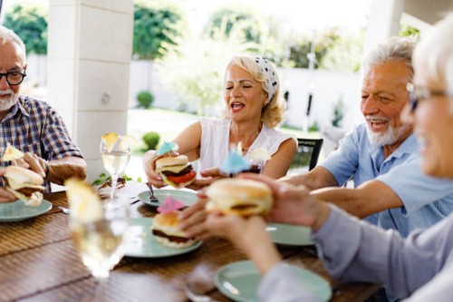 happy senior friends having burgers for snack on a party at patio. - junk food stock pictures, royalty-free photos & images