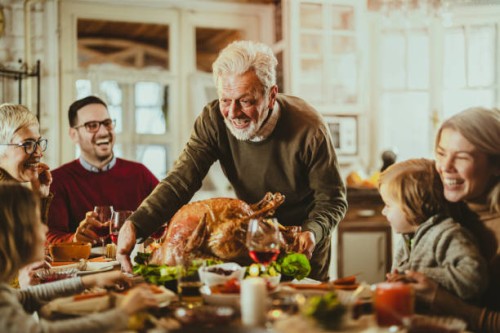 happy senior man serving thanksgiving turkey for his family at dining table. - home decoration stock pictures, royalty-free photos & images