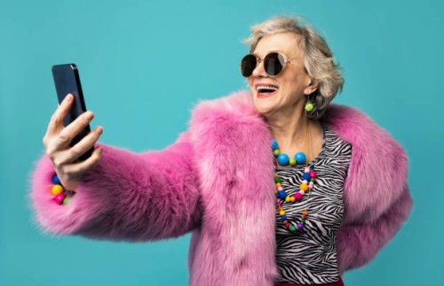happy senior woman wearing jewelry taking selfie through smart phone against turquoise background - fashion stock pictures, royalty-free photos & images
