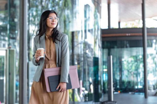 happy successful asian businesswoman holding a takeaway coffee cup and files on the street next to a glass building - junk food stock pictures, royalty-free photos & images