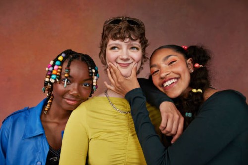 happy teenage female friends standing against brown background - fashion fotografías e imágenes de stock
