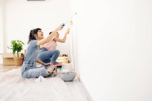 happy twin sisters painting walls while moving into their new apartment - home decoration stock pictures, royalty-free photos & images