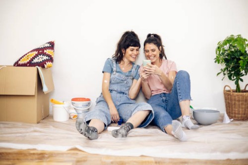 happy twins taking a break while painting at home and using a smartphone - home decoration stock pictures, royalty-free photos & images