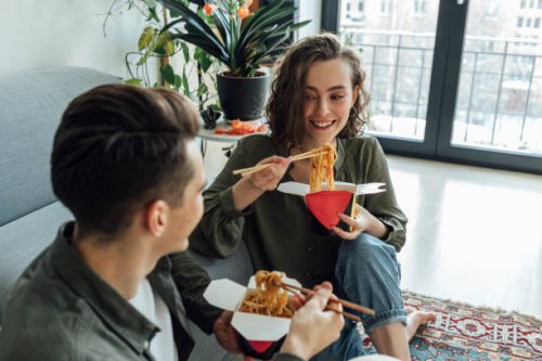 happy woman and man with take out food talking in living room at home - junk food stock pictures, royalty-free photos & images