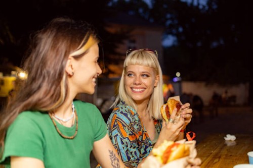 happy woman eating and talking to her friend on a music festival by night. - junk food stock pictures, royalty-free photos & images