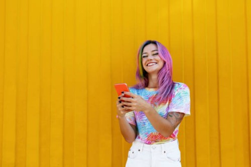 happy woman holding mobile phone in front of yellow wall - fashion stock pictures, royalty-free photos & images
