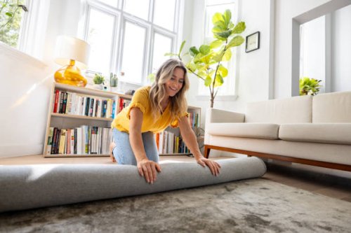 happy woman moving house and unrolling a carpet while unpacking - home decoration stock pictures, royalty-free photos & images