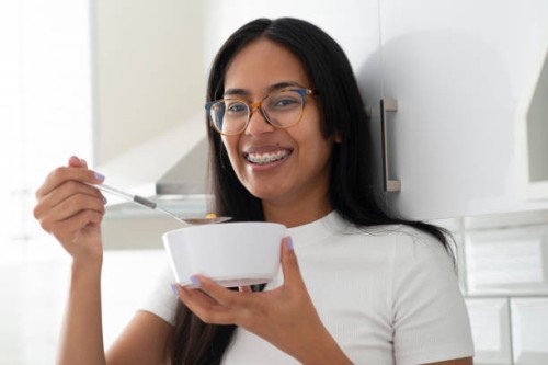 happy woman, portrait and eating porridge in bowl for morning, breakfast or meal in kitchen at home. face of female person smile with glasses for delicious snack, fiber or calcium vitamins at house - food stock pictures, roya