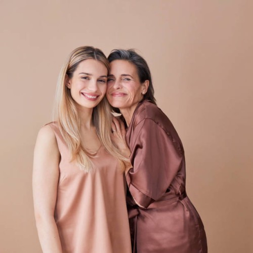 happy woman standing cheek to cheek with daughter against beige background - fashion stock pictures, royalty-free photos & images
