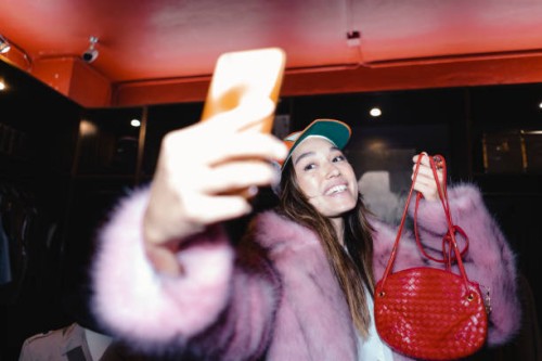 happy woman taking selfie through smart phone while wearing fur jacket and holding leather purse in store - fashion stock pictures, royalty-free photos & images
