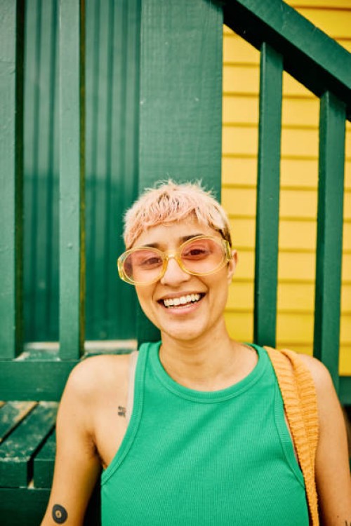 happy woman wearing green top and posing against the backdrop of a beach hut. - fashion stock pictures, royalty-free photos & images