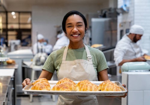 happy woman working at a bakery holding a tray of fresh bread - food stock pictures, royalty-free photos & images