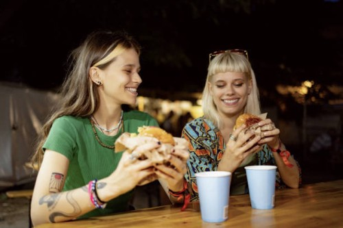 happy women eating burgers on a music festival at night. - concert stock pictures, royalty-free photos & images
