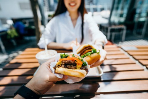 happy young asian couple eating beef burger with fries in an outdoor fast food restaurant - junk food stock pictures, royalty-free photos & images
