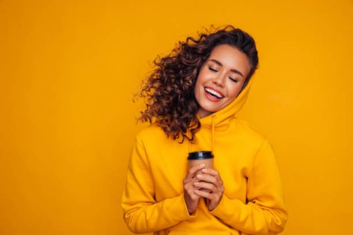 happy young cheerful girl laughing and holding cup of coffee on colored yellow background - fashion stock pictures, royalty-free photos & images