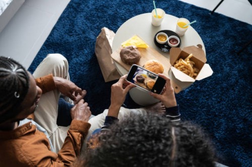 happy young couple eating fast food and filming it on mobile phone at home - junk food stock pictures, royalty-free photos & images