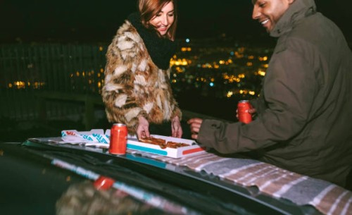 happy young couple having pizza on car bonnet against cityscape during night - junk food stock pictures, royalty-free photos & images