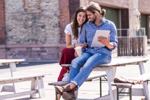 happy young couple sitting on table in a beer garden with tablet - junk food stock pictures, royalty-free photos & images