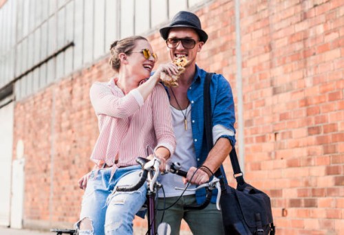 happy young couple with bicycle sharing a snack - fashion stock pictures, royalty-free photos & images