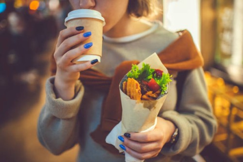 happy young girl drinking tea of coffee with street food in the evening city in summer - junk food stock pictures, royalty-free photos & images