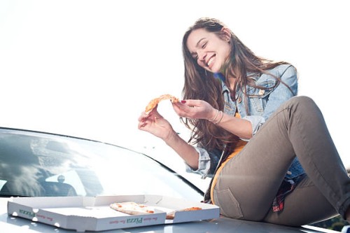 happy young woman eating pizza on car hood - junk food stock pictures, royalty-free photos & images