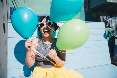 happy young woman holding balloons while sitting on bench - fashion photos et images de collection