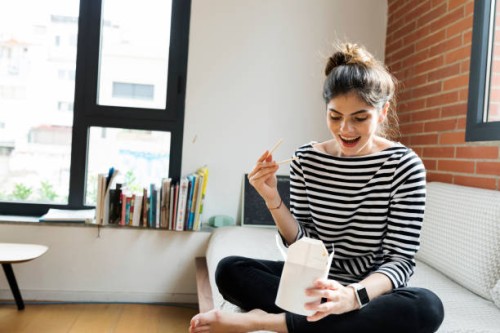 happy young woman sitting on couch at home having asian takeaway food - junk food stock pictures, royalty-free photos & images