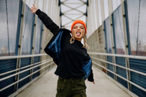 happy young woman with eyes closed sticking out tongue while dancing on footbridge - fashion stock pictures, royalty-free photos & images