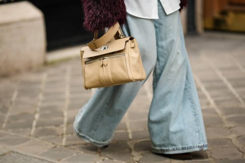 Heart Evangelista wears pale blue wide-leg flared denim pants / jeans, a beige leather Hermes bag large bag, during a street style fashion photo...