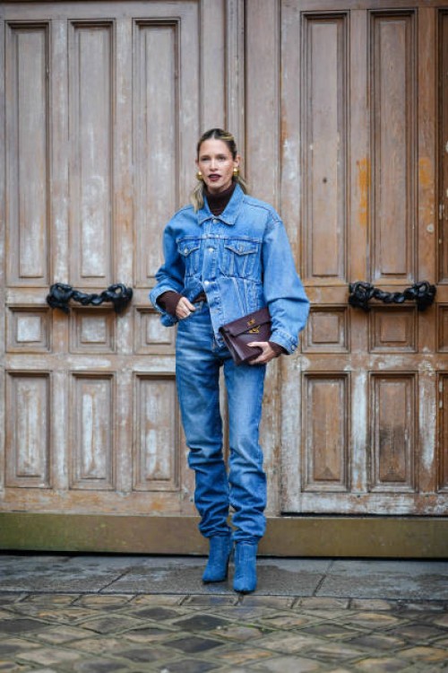 Helena Bordon wears golden earrings, lipstick, a brown turtleneck pullover , a blue oversized denim jacket, blue gathered denim pants / jeans ,...