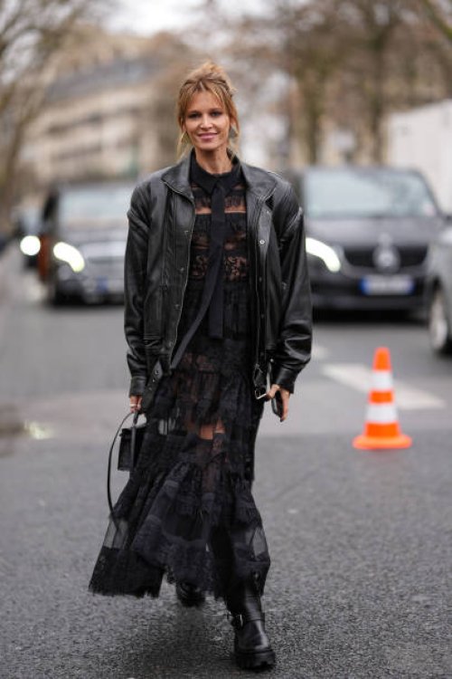 Helena Bordon wears silver earrings, a black leather oversized jacket, a black long lace dress, a black leather bag, black leather shoes, outside...