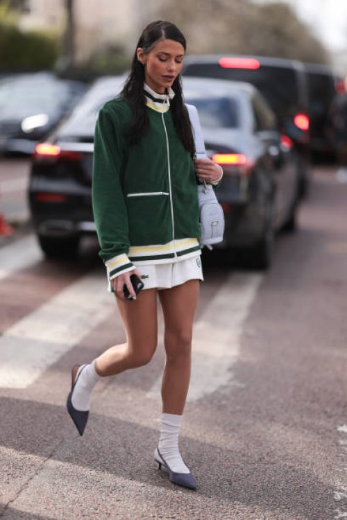 Heloise Agostinelli seen wearing a green and white Lacoste tennis skirt, green Lacoste jacket, white socks, grey heels, Lacoste white leather bag...
