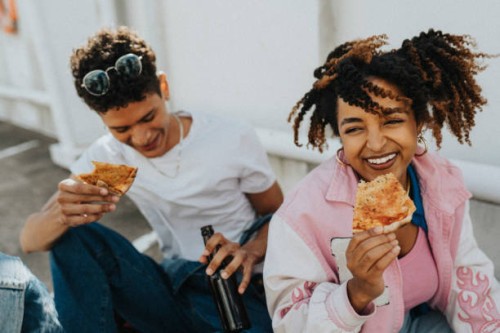 high angle view of curly hair woman eating pizza with male friend while sitting at parking lot - junk food stock pictures, royalty-free photos & images